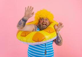 grasa temeroso hombre con peluca en cabeza es Listo a nadar con un rosquilla salvador de la vida foto