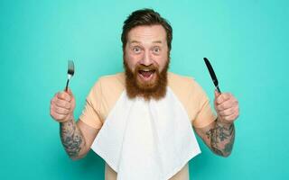 Man with tattoos is ready to eat with cutlery in hand. cyan background photo