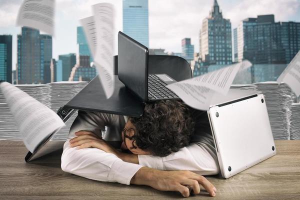 Tired businessman sleeping under a pile of laptops due to workload