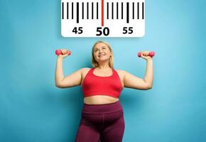 Fat girl does gym at home with satisfied expression because she decrease her weight. Cyan background photo