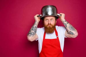 worried chef with beard and red apron plays with pot photo