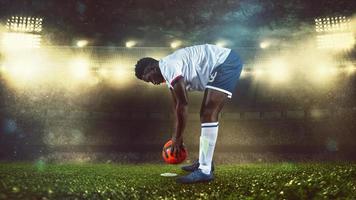 Soccer scene at night match with player in white and uniform placing the ball to kick photo