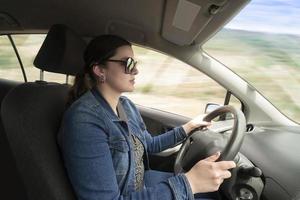joven latín mujer vestido en azul con lentes conducción su coche a alto velocidad durante el día foto