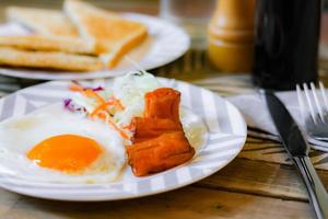Breakfast, fried eggs, fried sausage, vegetable salad and toast on a brown wooden table with coffee. photo