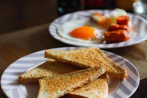 desayuno, frito huevos, frito embutido, vegetal ensalada y brindis en un marrón de madera mesa con café.