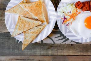 Breakfast, fried eggs, fried sausage, vegetable salad and toast on a brown wooden table with coffee. photo