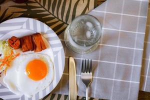 Breakfast, fried eggs, fried sausage, vegetable salad and toast on a brown wooden table with coffee. photo