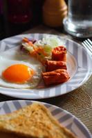 Breakfast, fried eggs, fried sausage, vegetable salad and toast on a brown wooden table with coffee. photo