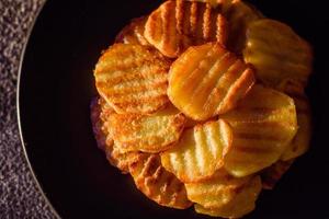 Delicious crispy fried potatoes in slices on a black ceramic plate photo