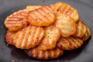 Delicious crispy fried potatoes in slices on a black ceramic plate photo