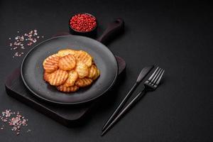 Delicious crispy fried potatoes in slices on a black ceramic plate photo