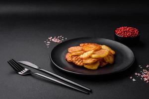 Delicious crispy fried potatoes in slices on a black ceramic plate photo