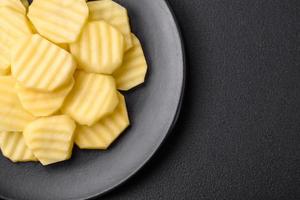 Raw fresh potatoes cut into slices on a black ceramic plate photo