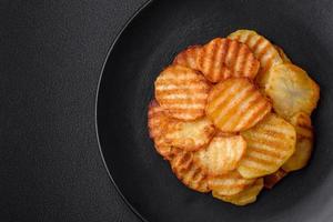 delicioso crujiente frito patatas en rebanadas en un negro cerámico plato foto