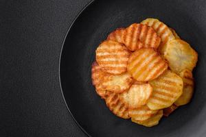 Delicious crispy fried potatoes in slices on a black ceramic plate photo