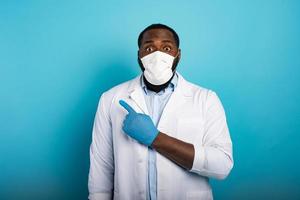 Worried medic with mask indicates something with hand. Blue background photo