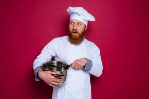 escéptico cocinero con barba y rojo delantal es Listo a cocinar foto