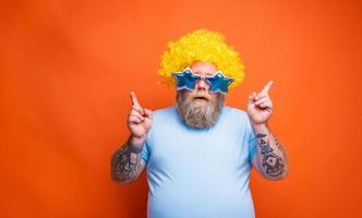 Fat thoughtful man with beard, tattoos and sunglasses dances music on a disco photo