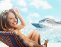 Beautiful girl sitting on a deck chair at the beach at sunset with cruiseship on background photo