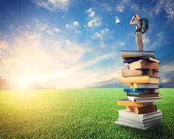 Man with binoculars over a pile of books observe a colorful sunrise. the culture open the imagination photo