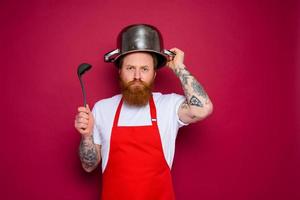 unhappy chef with beard and red apron plays with pot photo