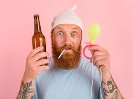 Amazed man with beard and tattoos acts like a little newborn baby with beer in hand photo