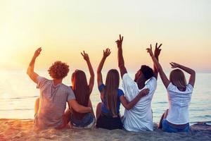 Group of happy friends having fun at ocean beach at dawn photo