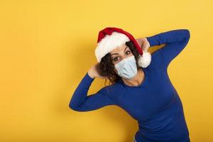 Happy woman with Christmas hat and face mask to be protect against covid-19. Yelow background photo