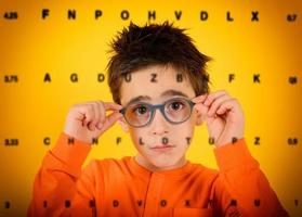 Child tries new glasses to see better. yellow background photo