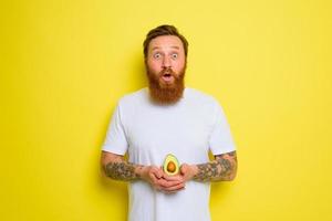 Amazed with beard and tattoos holds an avocado photo