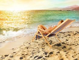 niña bronceado en un cubierta silla en un hermosa playa foto