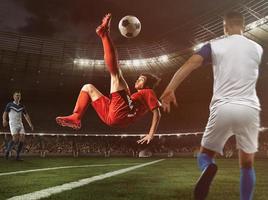 Soccer striker in red uniform hits the ball with an acrobatic kick in the air at the stadium photo