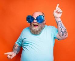 Fat happy man with beard, tattoos and sunglasses dances music photo