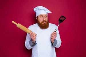 doubter chef with beard and red apron chef holds wooden rolling pin photo