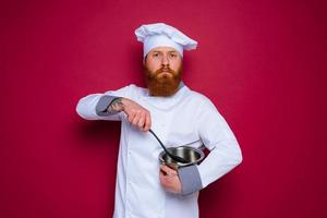 escéptico cocinero con barba y rojo delantal es Listo a cocinar foto