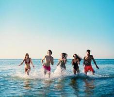 Group of friends run in the sea. Concept of summertime photo