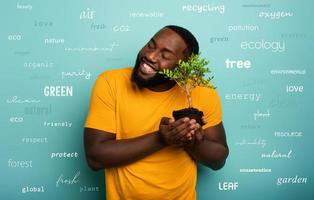 Happy boy hugs a small tree ready to be planted over a light blue color. Concept of forestation, ecology and conservation with most important terms photo