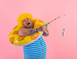 Fat stressed man with wig in head plays with the fishing rod photo