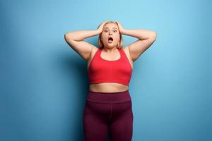 Fat girl in fitness suite wants to start a diet but has some. Cyan background photo