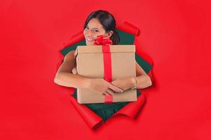 Woman inside a hole on a red paper backdrop holds tight in her arms a gift package photo