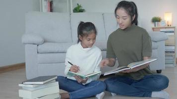 lección de enseñanza de madre para hija por computadora portátil. una niña asiática aprende en casa. hacer la tarea con la amable ayuda de la madre, animar para el examen. niña de asia feliz educación en el hogar. mamá aconseja educación juntos. video