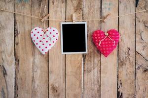 Two heart and photo frame hanging on clothesline rope with wooden background.