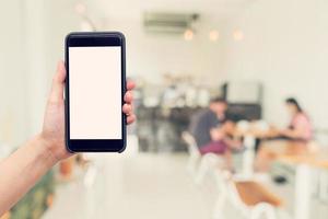 mano mujer participación teléfono con blanco pantalla y difuminar café tienda. foto