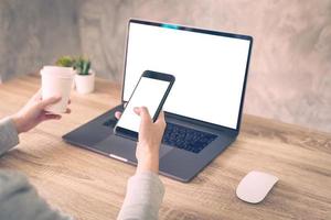 Hipster women holding phone and using laptop on wooden table in coffee shop. photo