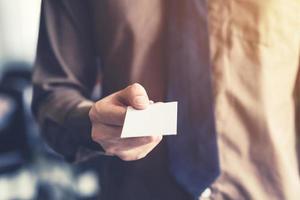 Business man holding white business card in the office. Vintage toned. photo