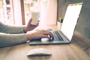 Woman holding coffee and using laptop on wooden table in office photo