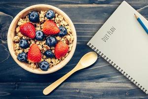Homemade granola and fresh berries on wood table with note book and text diet plan concept, copy space. photo