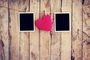 Red heart and two photo frame hanging on clothesline rope with wooden background.