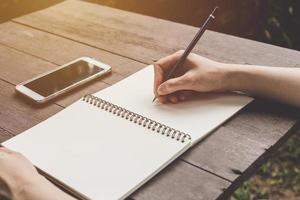 cerca arriba mano mujer escritura cuaderno en madera mesa antecedentes. foto