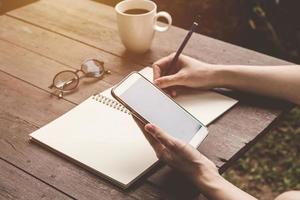 close up hand woman writing notebook and holding phone on wood table backhround with vintage toned. photo